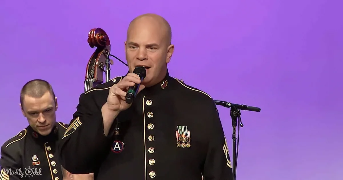 A man in military uniform sings into a microphone, adorned with medals, against a purple backdrop.