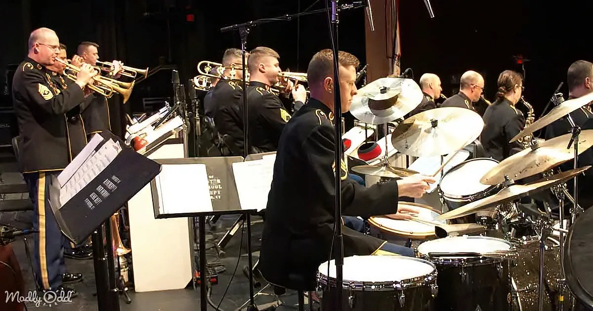 A military band in uniform plays brass and percussion instruments on stage.