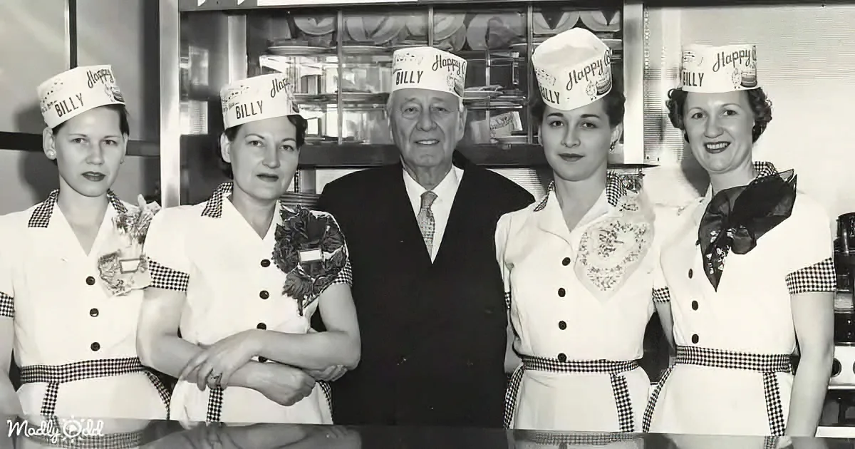 A man in a suit stands with four women in uniform, all wearing "Billy" hats, in a vintage setting.