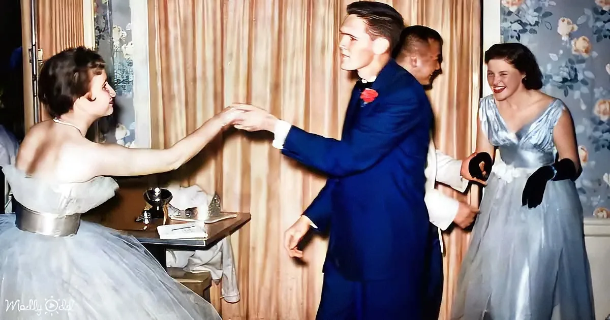 A man in a blue suit dances with a woman in a light blue dress, holding hands, while another woman in a similar dress...