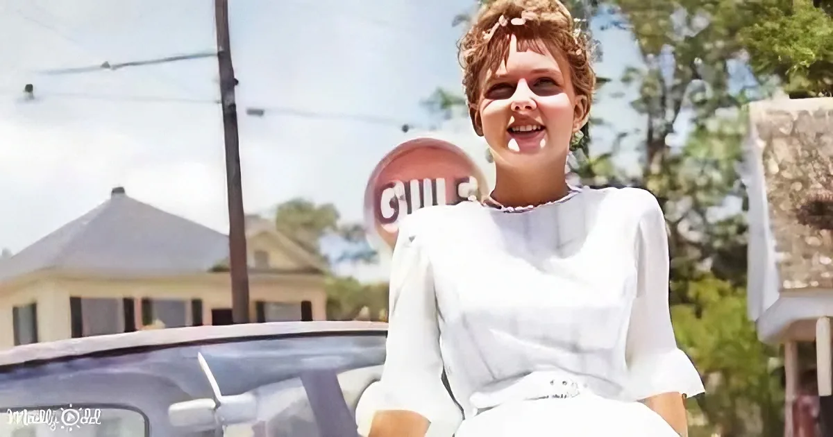 A woman in a white dress sits on a car, smiling, with a "Guil's" sign in the background.