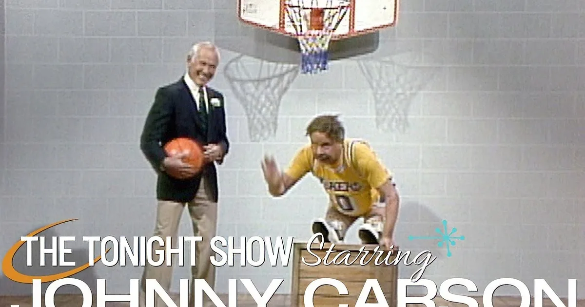 A man in a Lakers jersey is humorously holding a basketball hoop, while another man in a suit holds a basketball.