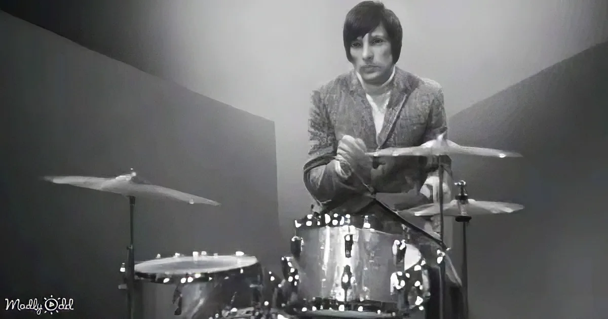 A man in a suit plays drums under a spotlight, creating a dramatic and focused scene.