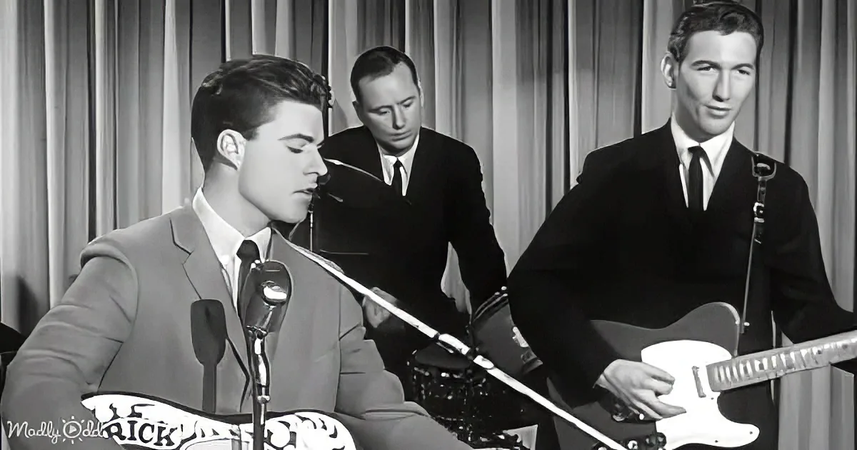 A man in a suit sings into a microphone, accompanied by a guitarist and drummer in a vintage setting.