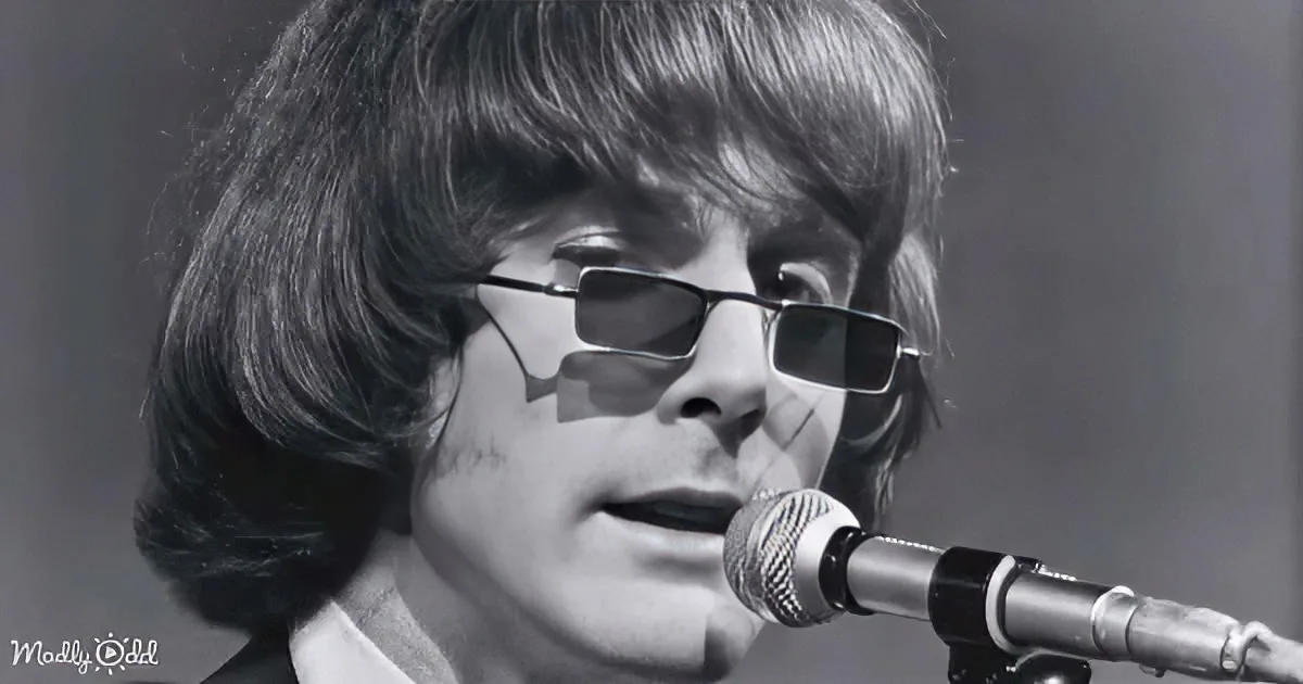 A person with long hair and sunglasses sings into a microphone, wearing a collared shirt.