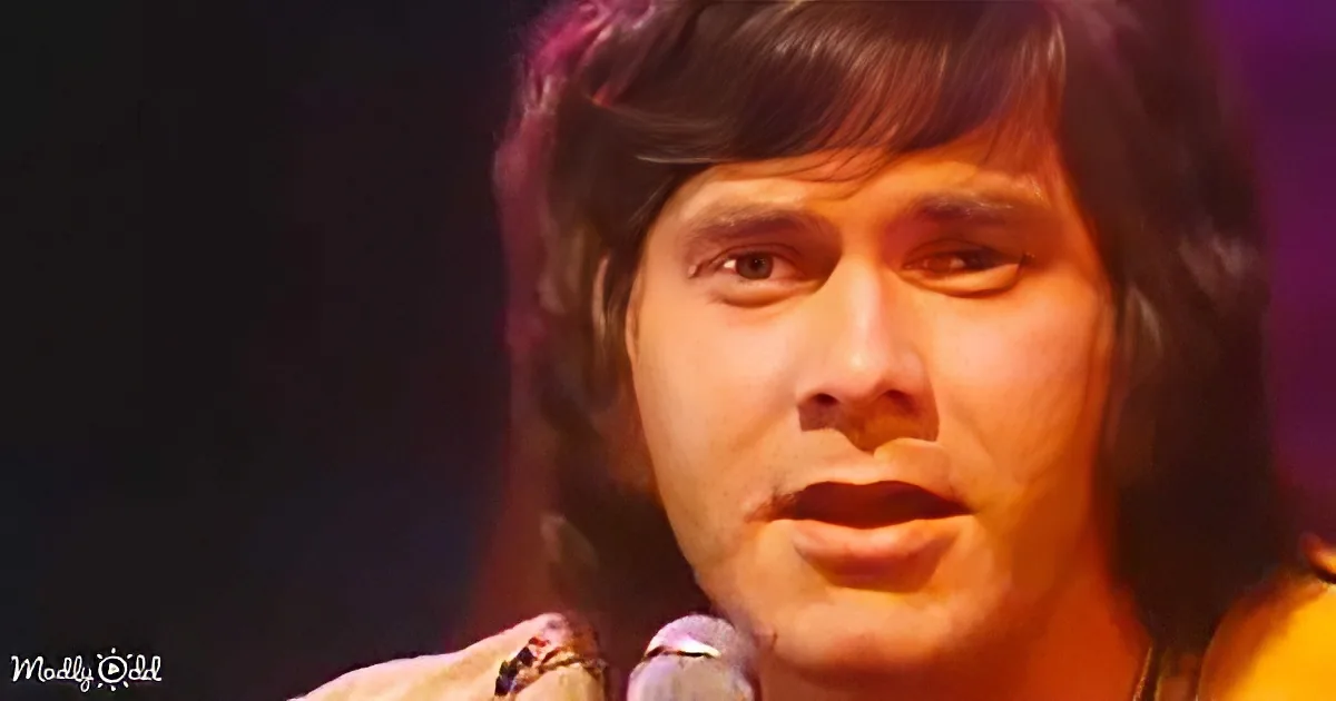 A person with dark hair and a light-colored shirt is singing into a microphone.