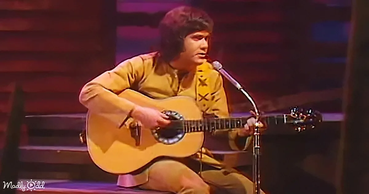 A person in a yellow shirt plays an acoustic guitar on stage with a microphone.