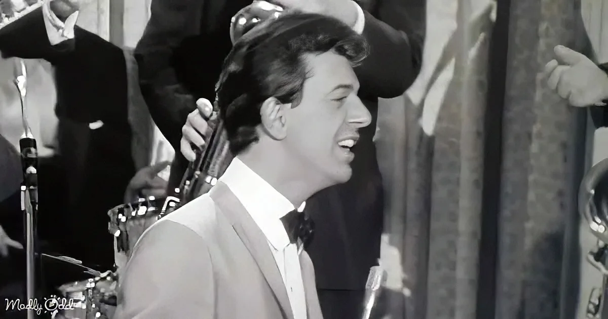 A man in a suit and bow tie smiles while playing a musical instrument in a band setting.