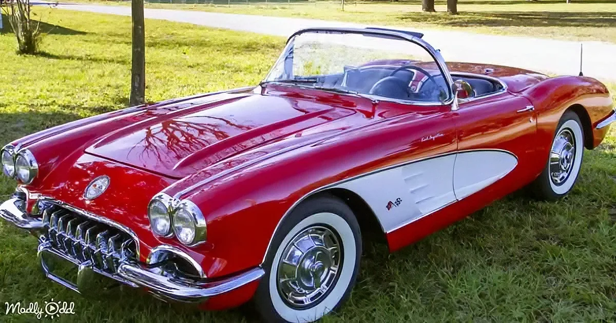 A classic red convertible sports car with white wall tires and chrome details sits on grass.