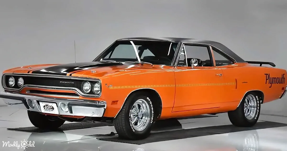 A vibrant orange 1970 Plymouth Road Runner with a black hood and racing stripes is showcased in a studio setting.