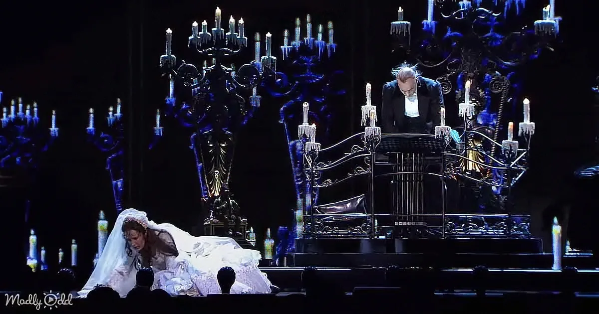 A bride in white lies on the ground, while a man in black stands beside a bed, surrounded by ornate candelabras.