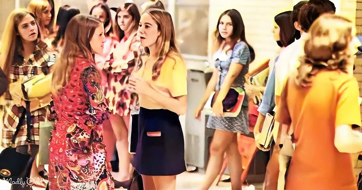 Two women in a crowded room, one in a floral dress and the other in a yellow top, appear to be having a conversation.