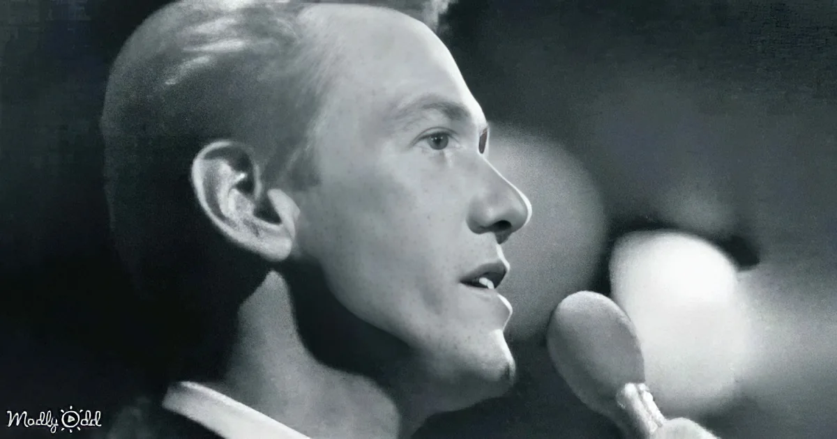 A man sings into a microphone, his head slightly tilted, in a black-and-white image.