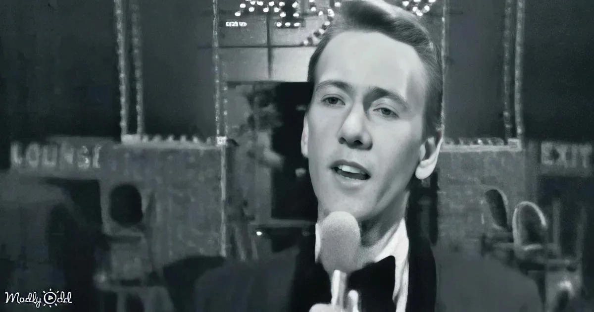 A man in a suit sings into a microphone, with a "Lounge" sign and blurred background.