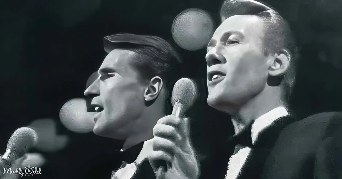 Two men in suits sing into microphones, one holding a microphone close to his mouth.