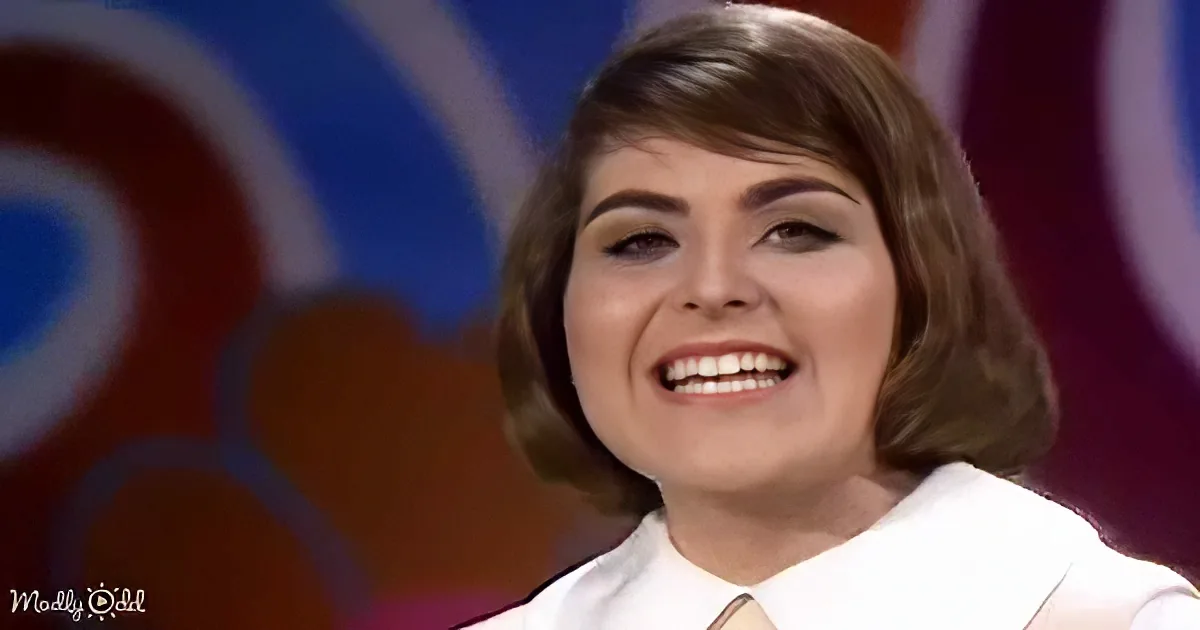 A smiling woman with shoulder-length hair, wearing a white shirt and striped tie, against a colorful background.
