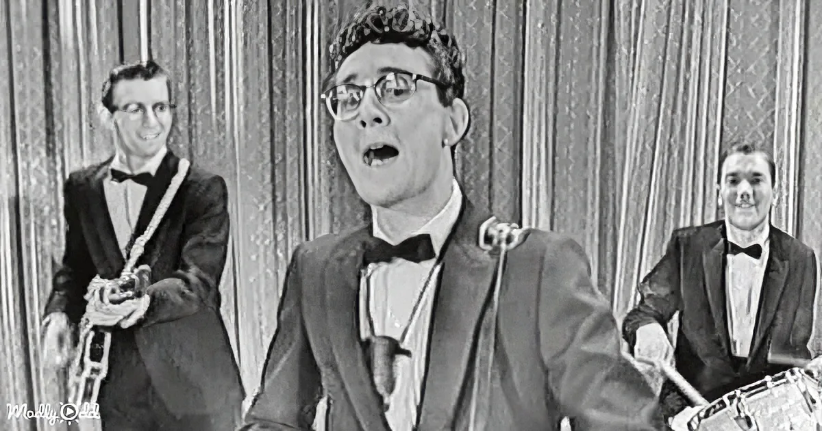 A man in a suit and bow tie sings passionately, flanked by two musicians with instruments, in a vintage setting.