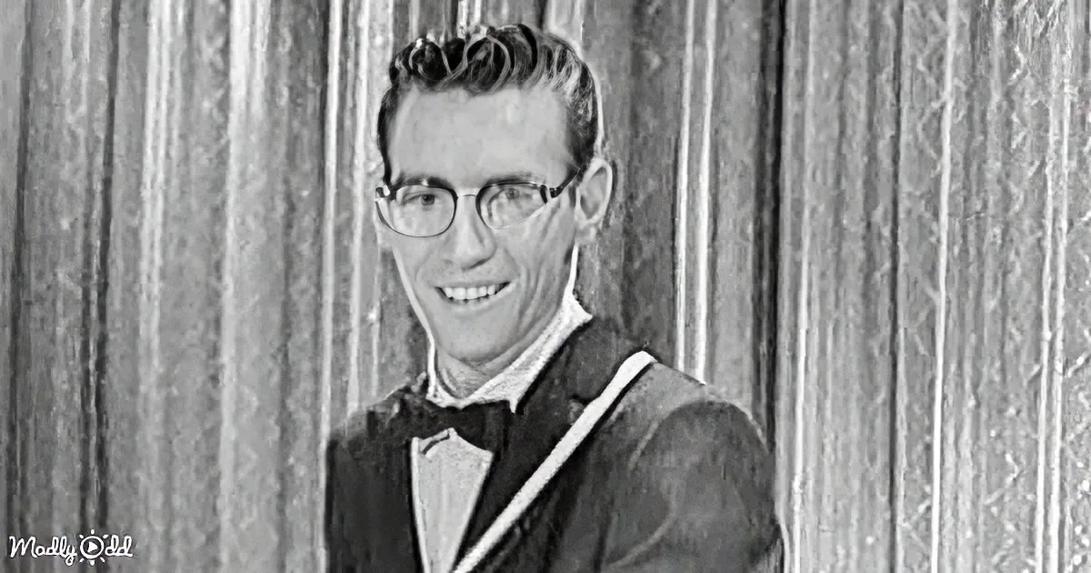 A man in a suit and bow tie smiles, wearing glasses, against a textured background.