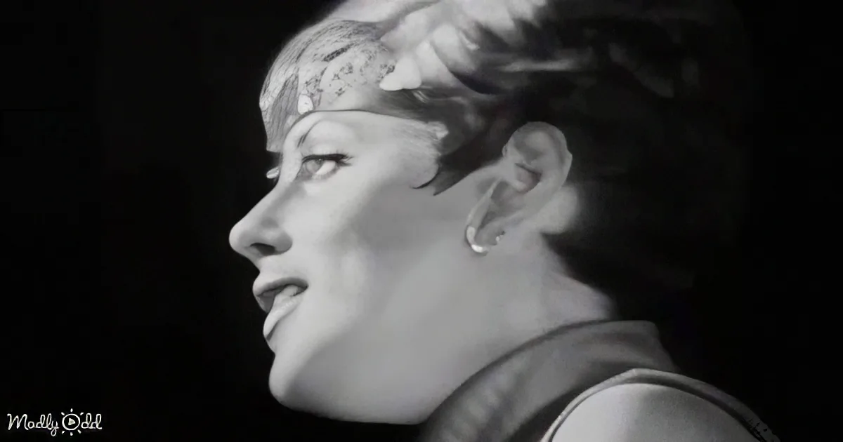 A side profile of a person with short hair, wearing a headband and earrings, against a dark background.