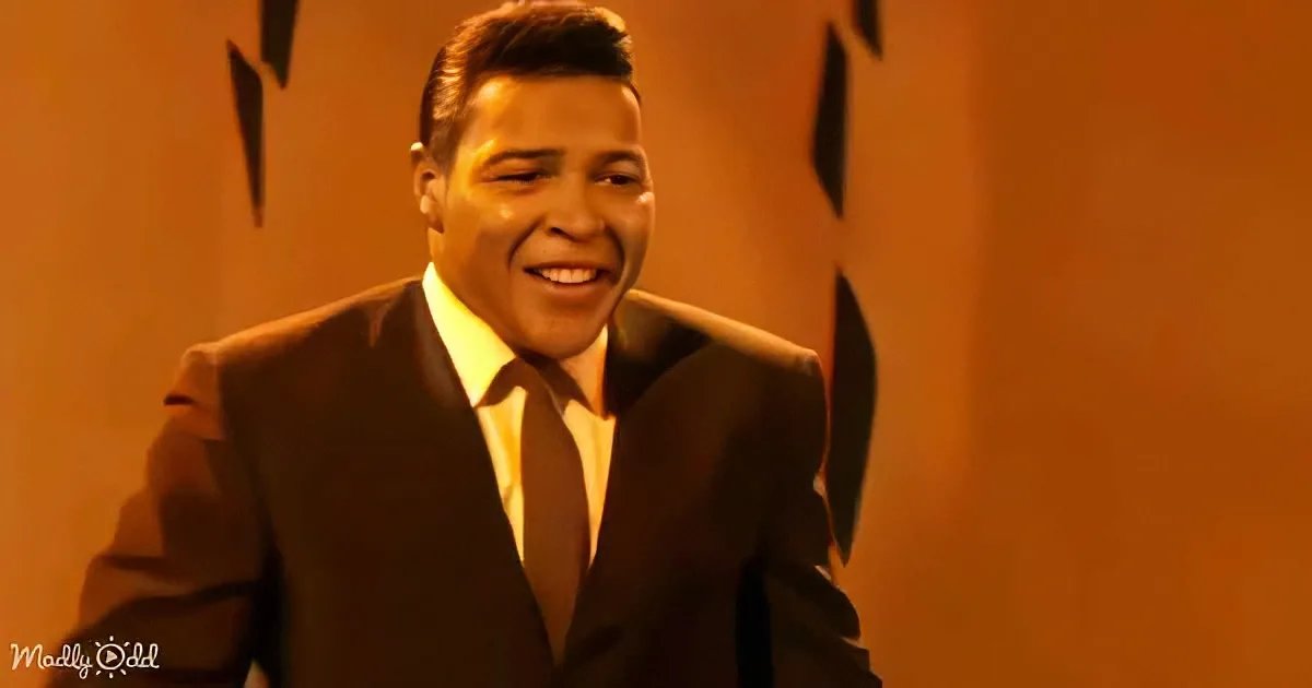 A man in a dark suit and tie smiles warmly against an orange background.