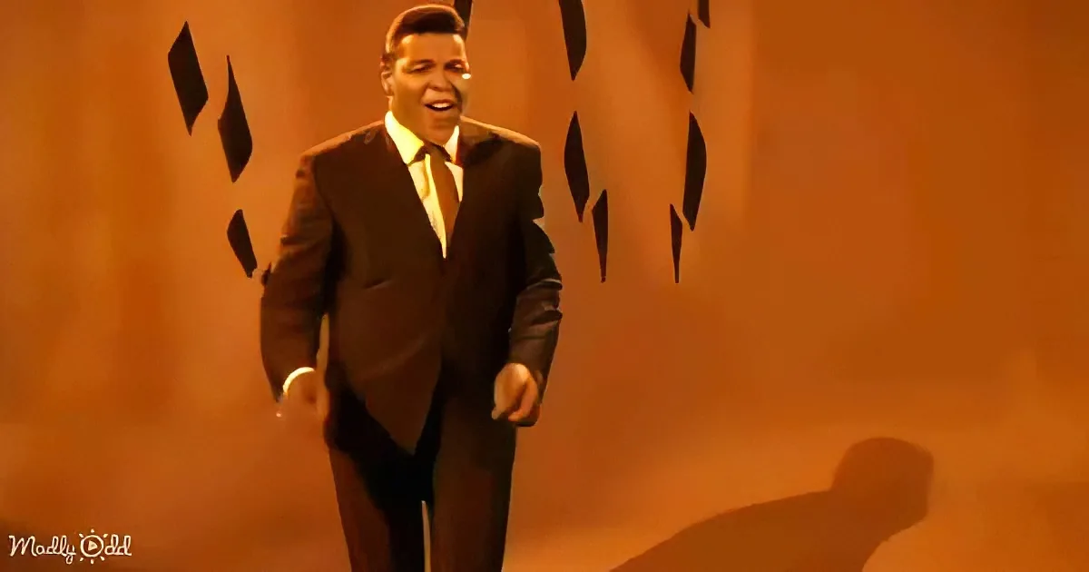 A man in a suit and hat is smiling, surrounded by black diamond shapes against an orange background.