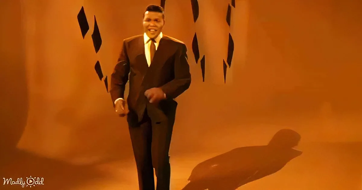 A man in a suit and tie stands confidently with a smile, casting a shadow on a warm-toned background.