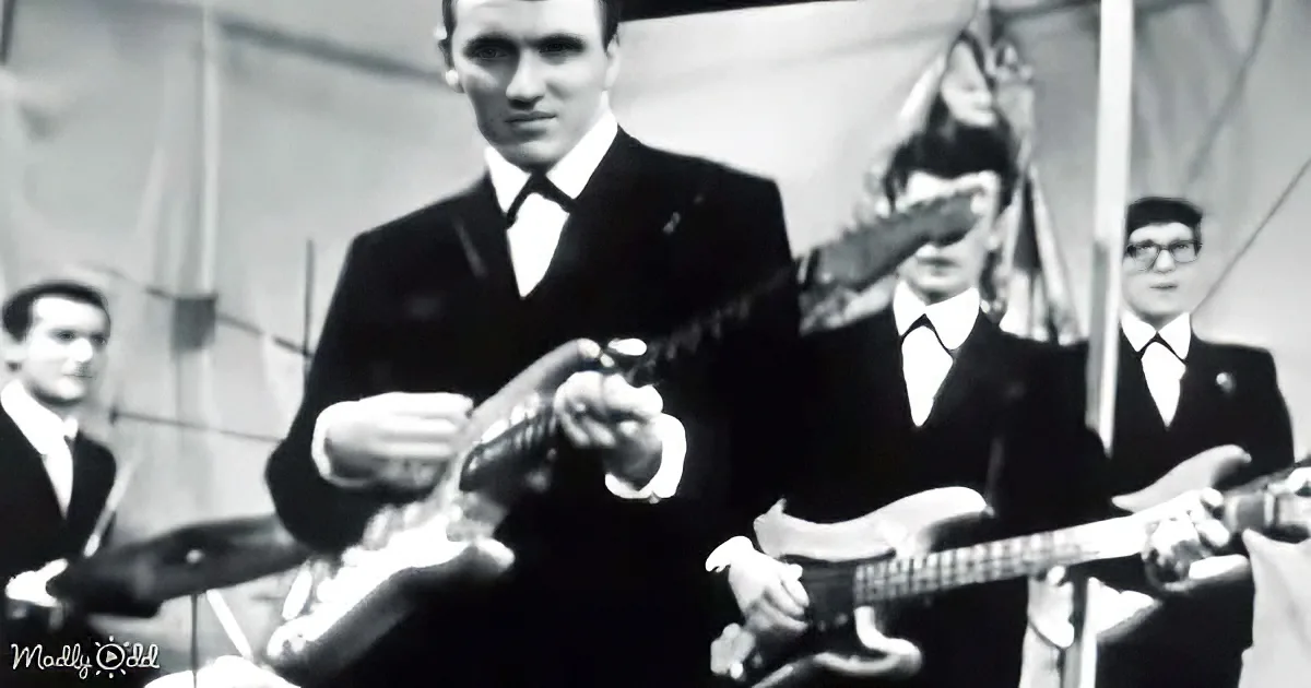 A man in a suit plays a guitar, surrounded by other musicians in a vintage setting.