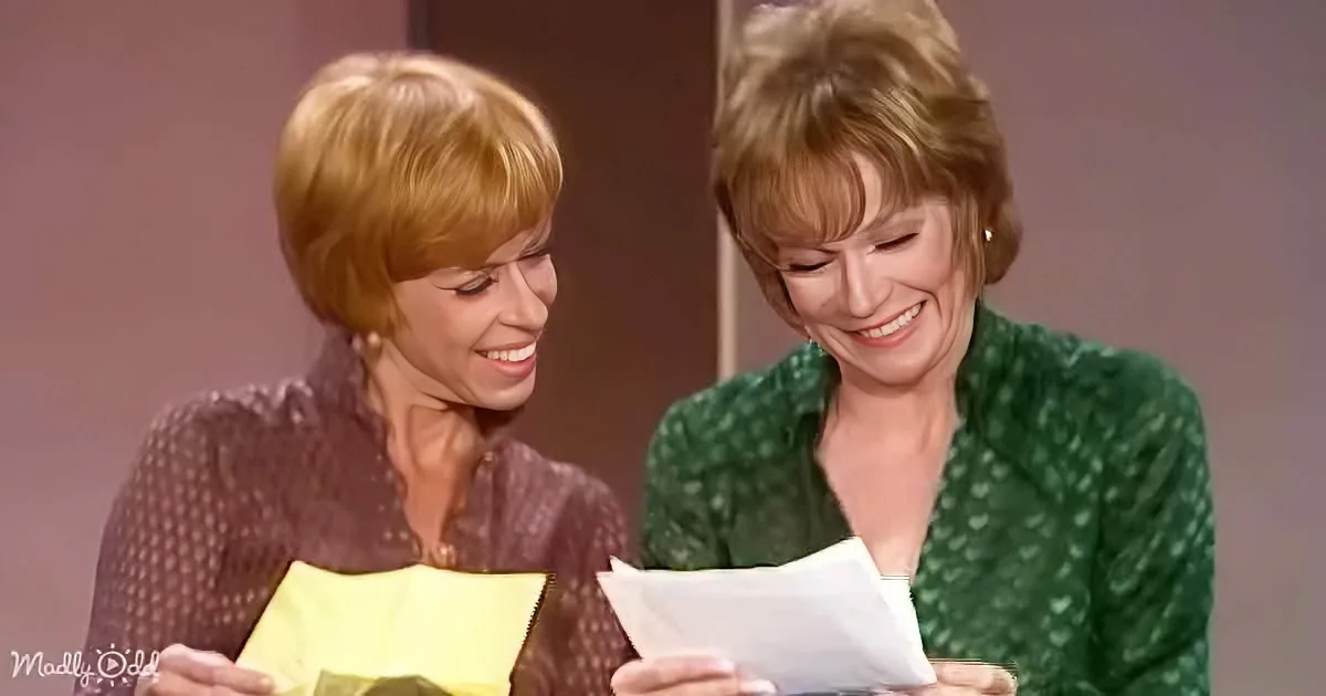 Two women, one in green, the other in brown, are smiling and holding papers, seemingly engaged in a conversation or activity.