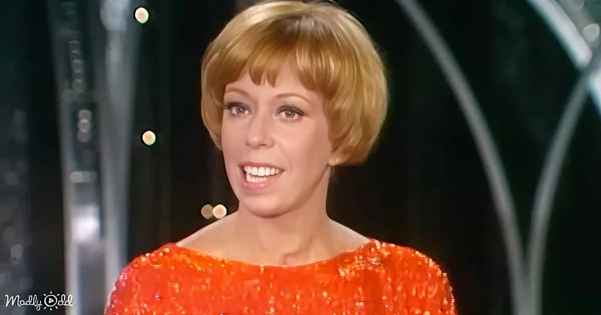 A woman with short blonde hair and a bright orange sequined dress smiles warmly.