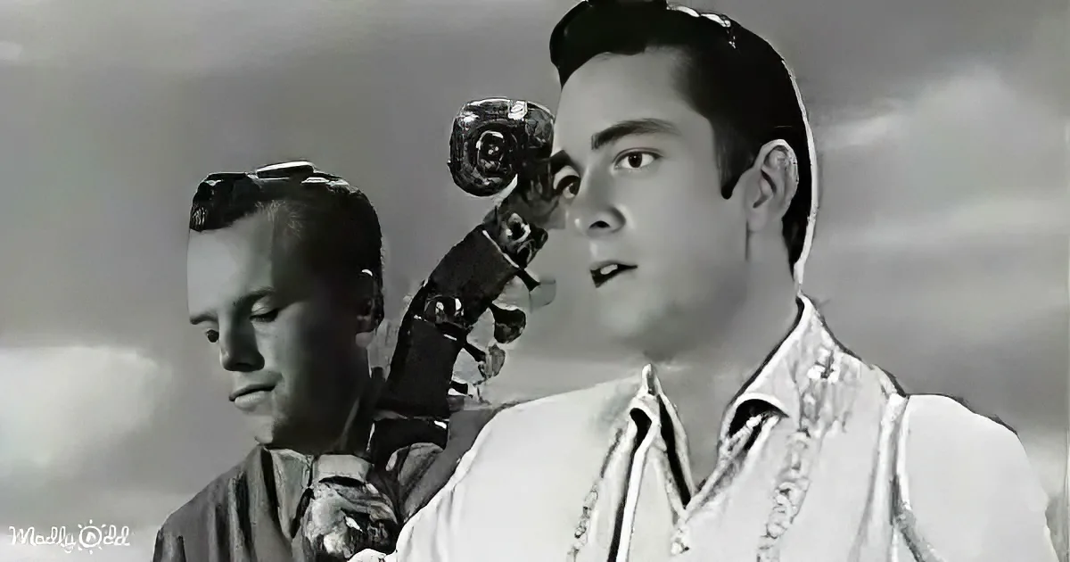 A man in a white shirt holds a violin, another man in a dark shirt looks down beside him.