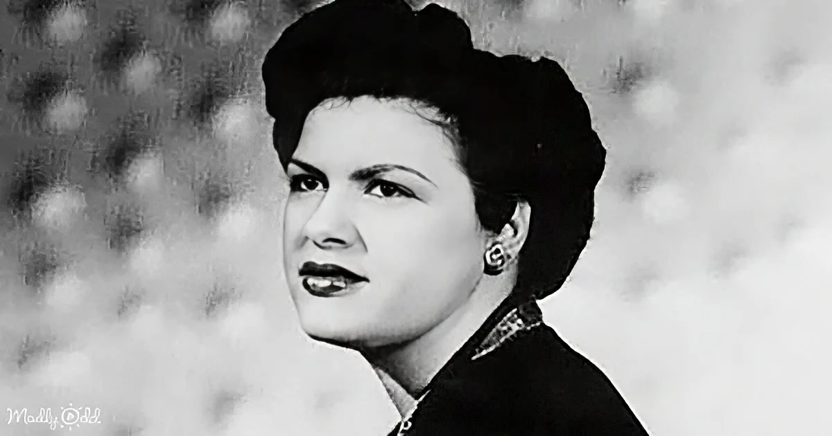 A woman with dark hair styled in a bun, wearing a dark outfit and earrings, gazing to the side.