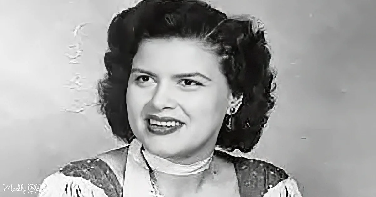 A woman with dark, styled hair and a white top smiles in a black-and-white portrait.