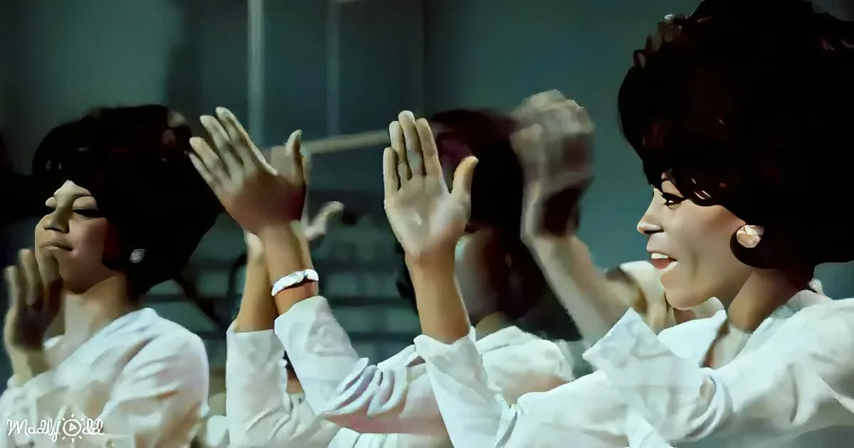 A group of women in white outfits raise their hands in a synchronized gesture.