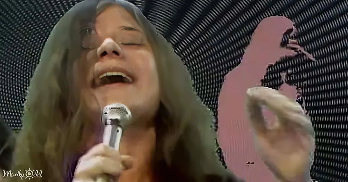 A person with long hair sings passionately into a microphone, wearing a white glove, with a pink silhouette in the...