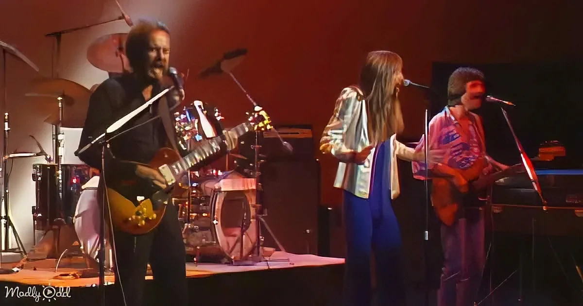 A band performs on stage with a guitarist, a singer, and a drummer in the background.