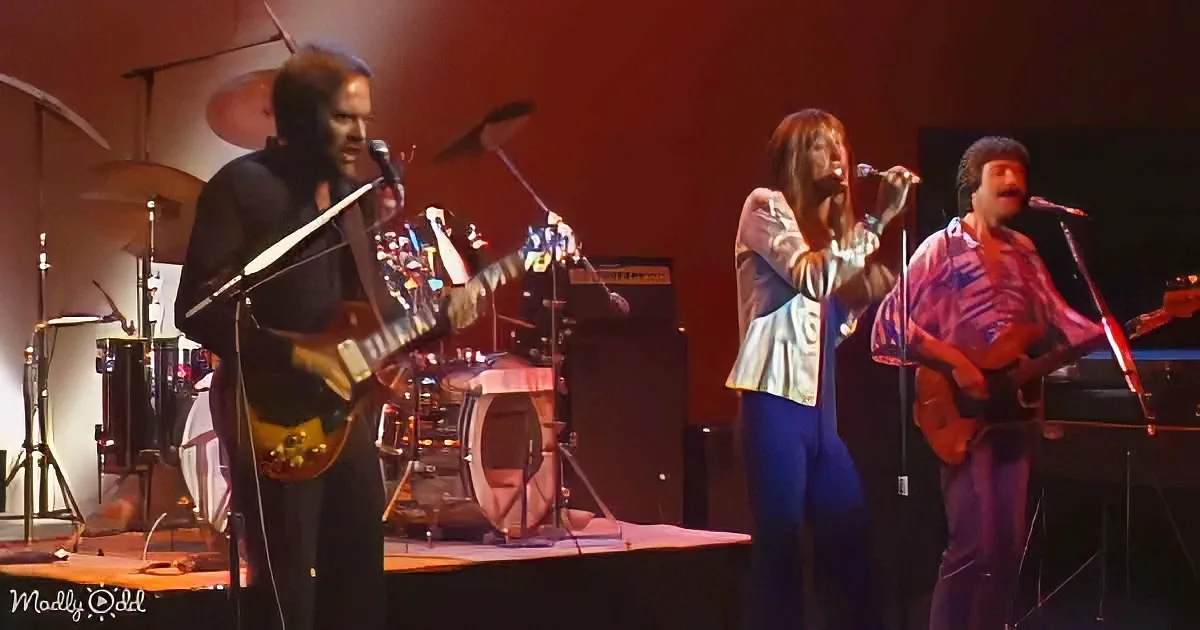A band performs on stage with a guitarist, drummer, and singer, illuminated by warm lighting.