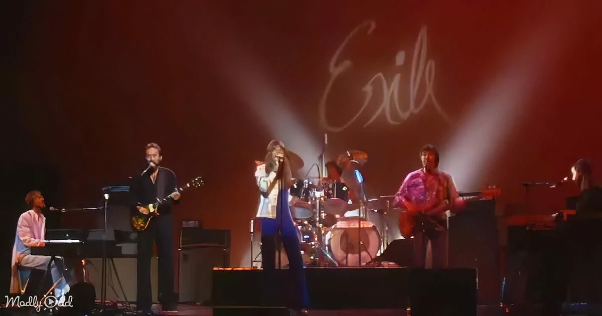 A band performs on stage with "Exile" projected in the background, featuring a keyboardist, guitarist, and vocalist.