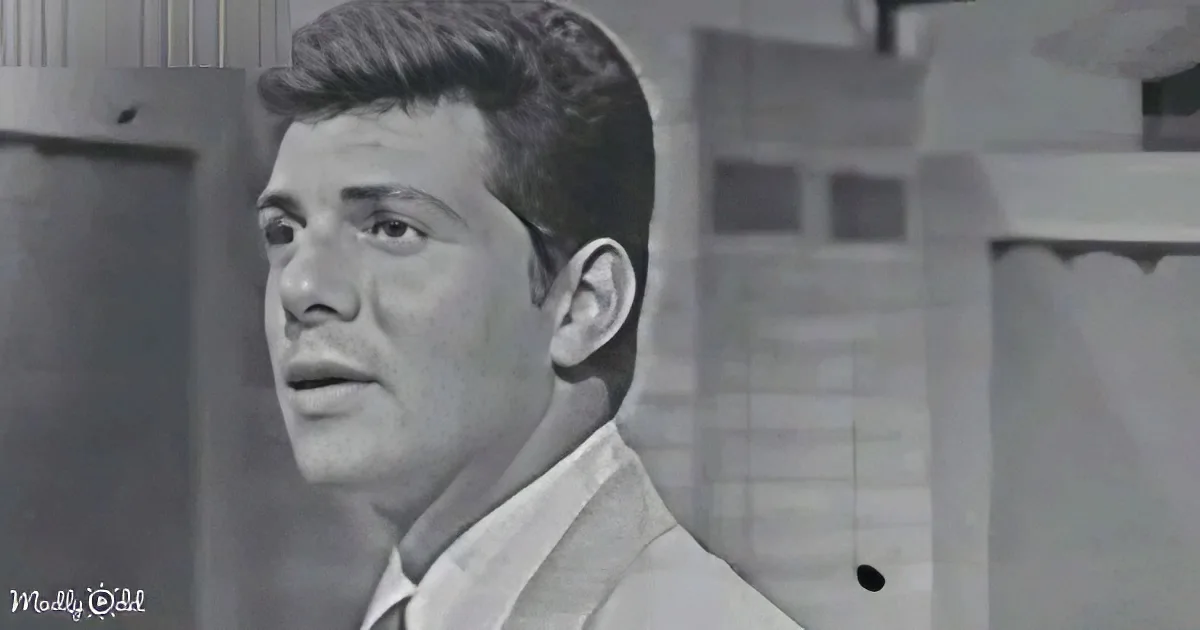 A man in a suit and tie looks to the side with a serious expression in a black-and-white setting.