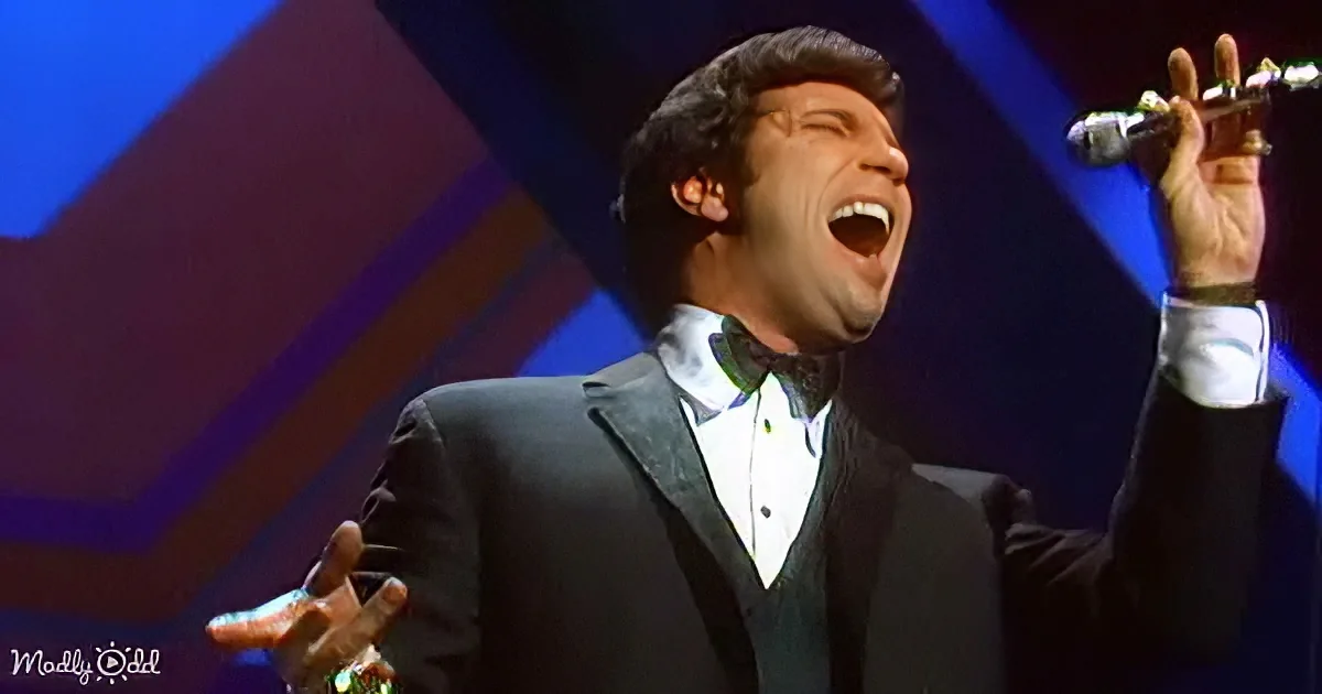 A man in a tuxedo sings passionately on stage with a microphone in hand.