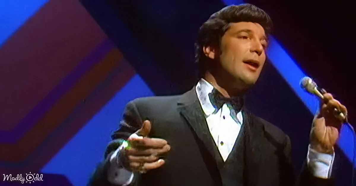 A man in a tuxedo sings passionately on stage, holding a microphone.