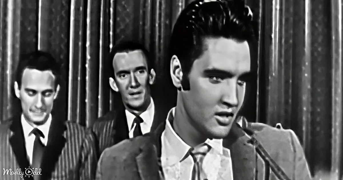 Elvis Presley sings passionately, flanked by two backup singers in a vintage black-and-white setting.
