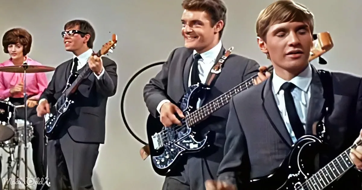 A band in suits plays guitars, with a drummer in the background, in a vintage setting.