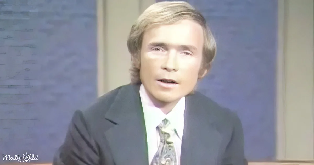 A man in a suit and tie, with blonde hair, appears to be speaking or presenting.