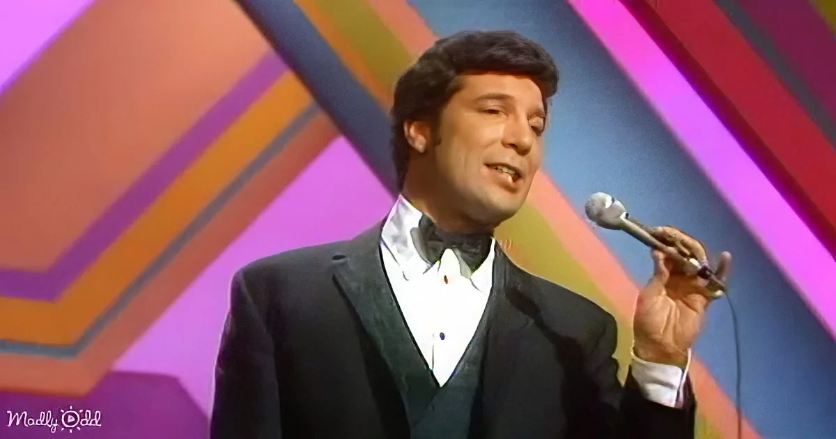 A man in a suit sings into a microphone on a colorful stage backdrop.