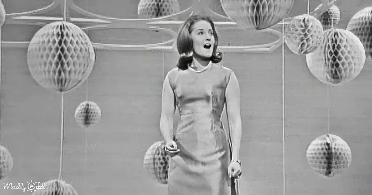 A woman in a 1960s dress stands in front of a wall decorated with hanging paper lanterns.