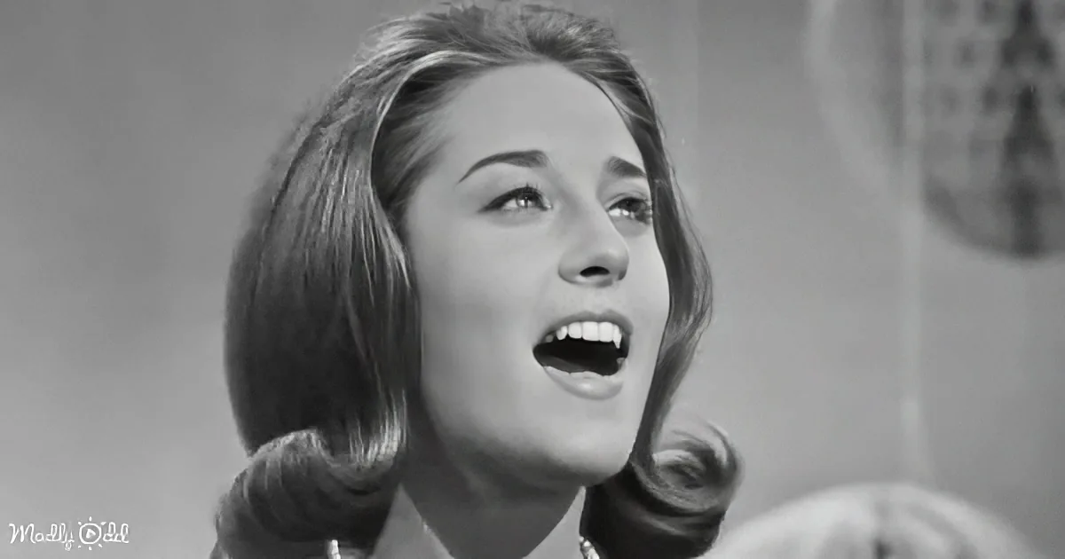 A woman with mid-length hair, wearing a turtleneck, is captured mid-expression, possibly singing or speaking.