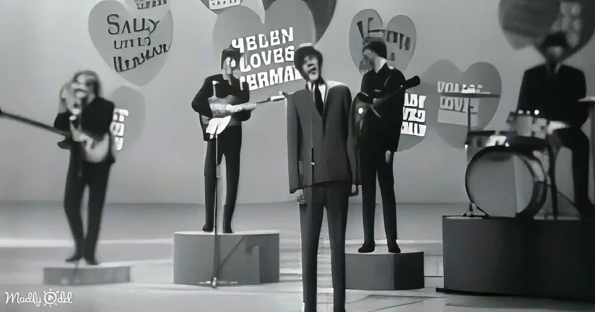 A man in a suit stands on a pedestal, singing passionately on stage with a band.