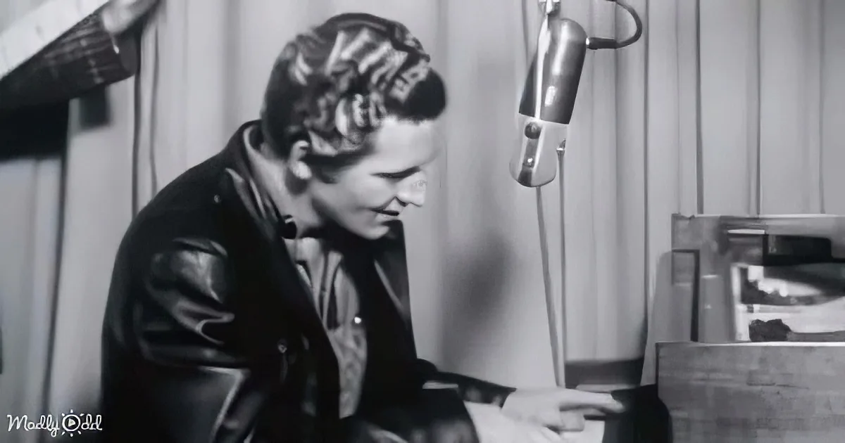 A woman in a leather jacket sits at a desk with a microphone, possibly recording or broadcasting.