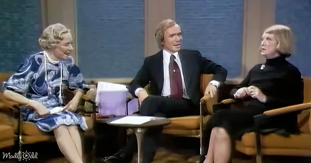 Three individuals are seated in chairs, engaged in a conversation, with a table in front of them.
