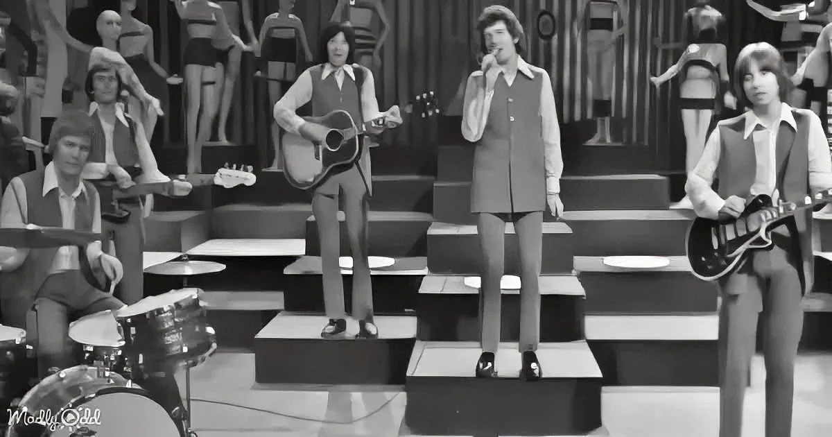 A band performs on stage with mannequins in the background, dressed in 1970s fashion.